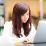 ノートパソコンでブログを書いている若い女性